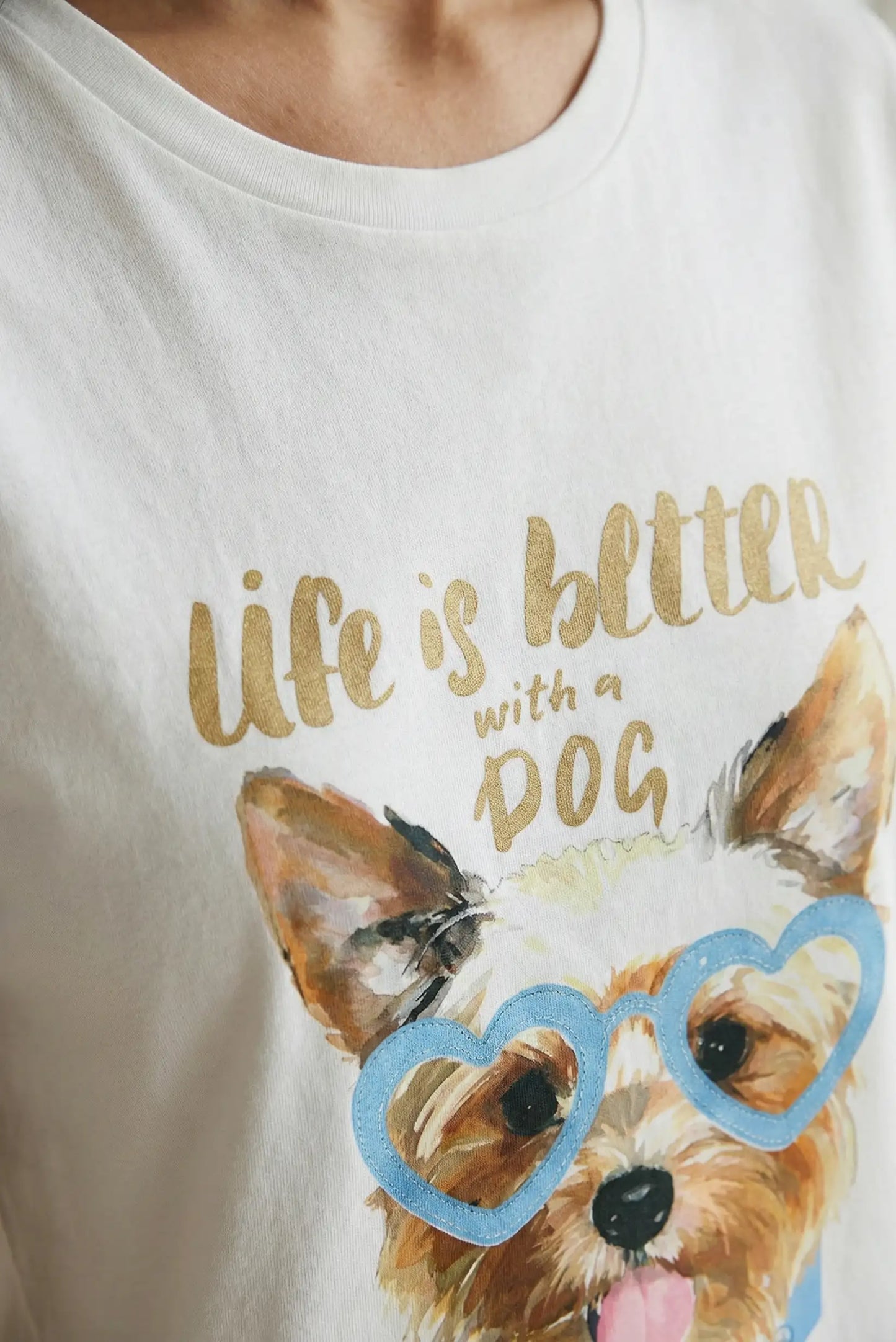 Camiseta blanca de mujer con ilustración de perro y gafas azules en forma de corazón, diseño casual.