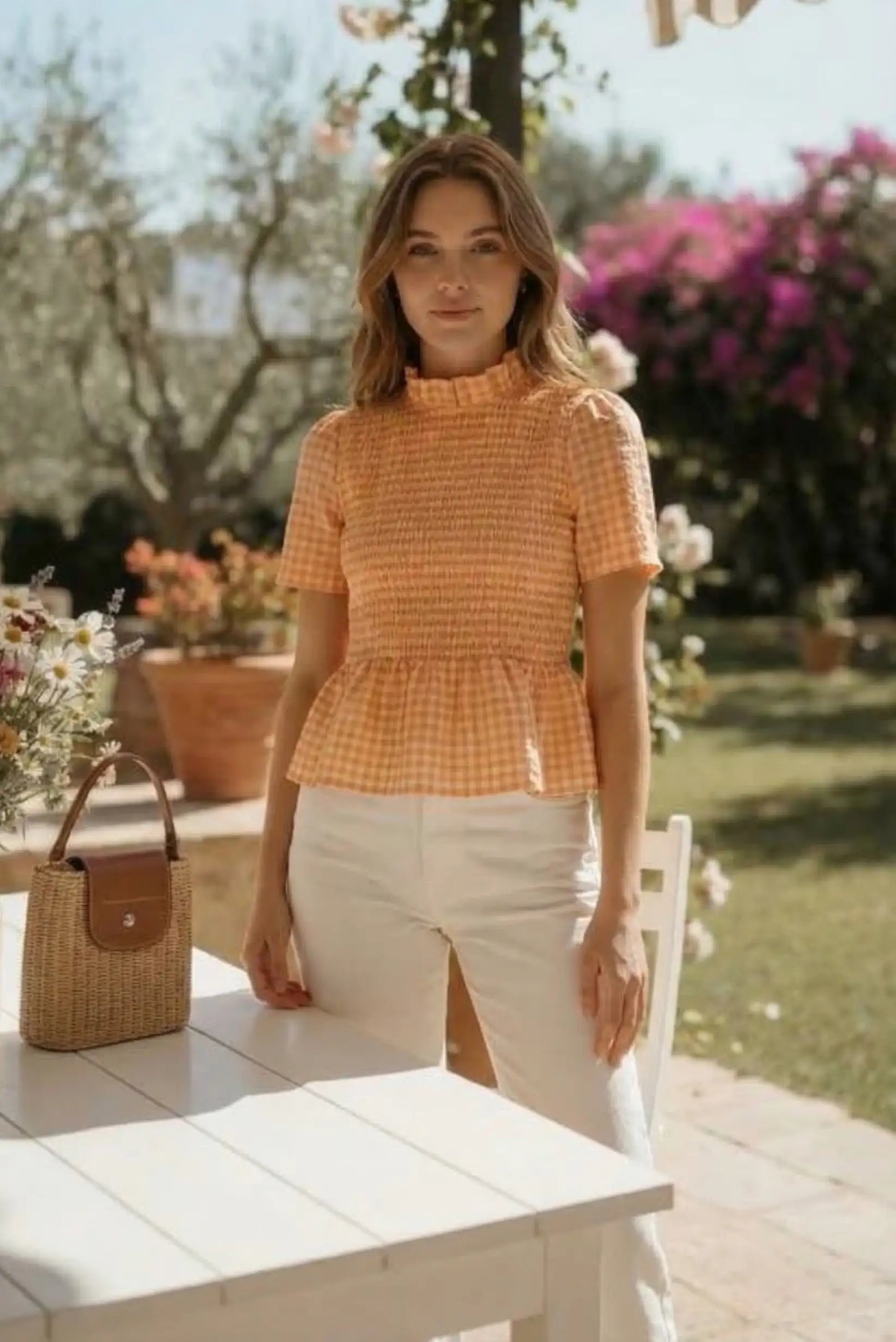 Mujer con camiseta fruncida de cuadros naranja y pantalón claro en un jardín soleado