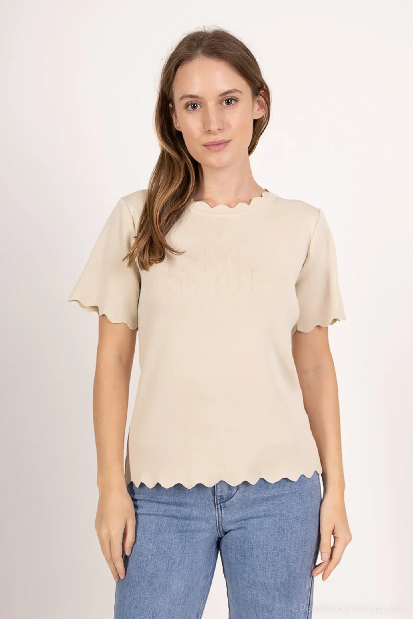 Mujer con camiseta beige de manga corta y cuello ondulado, combinada con jeans claros, moda casual.