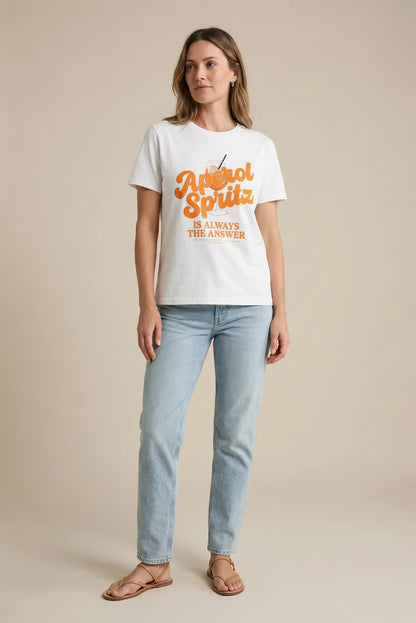 Mujer con camiseta blanca estampada de Aperol Spritz, jeans claros y sandalias, moda casual primavera.