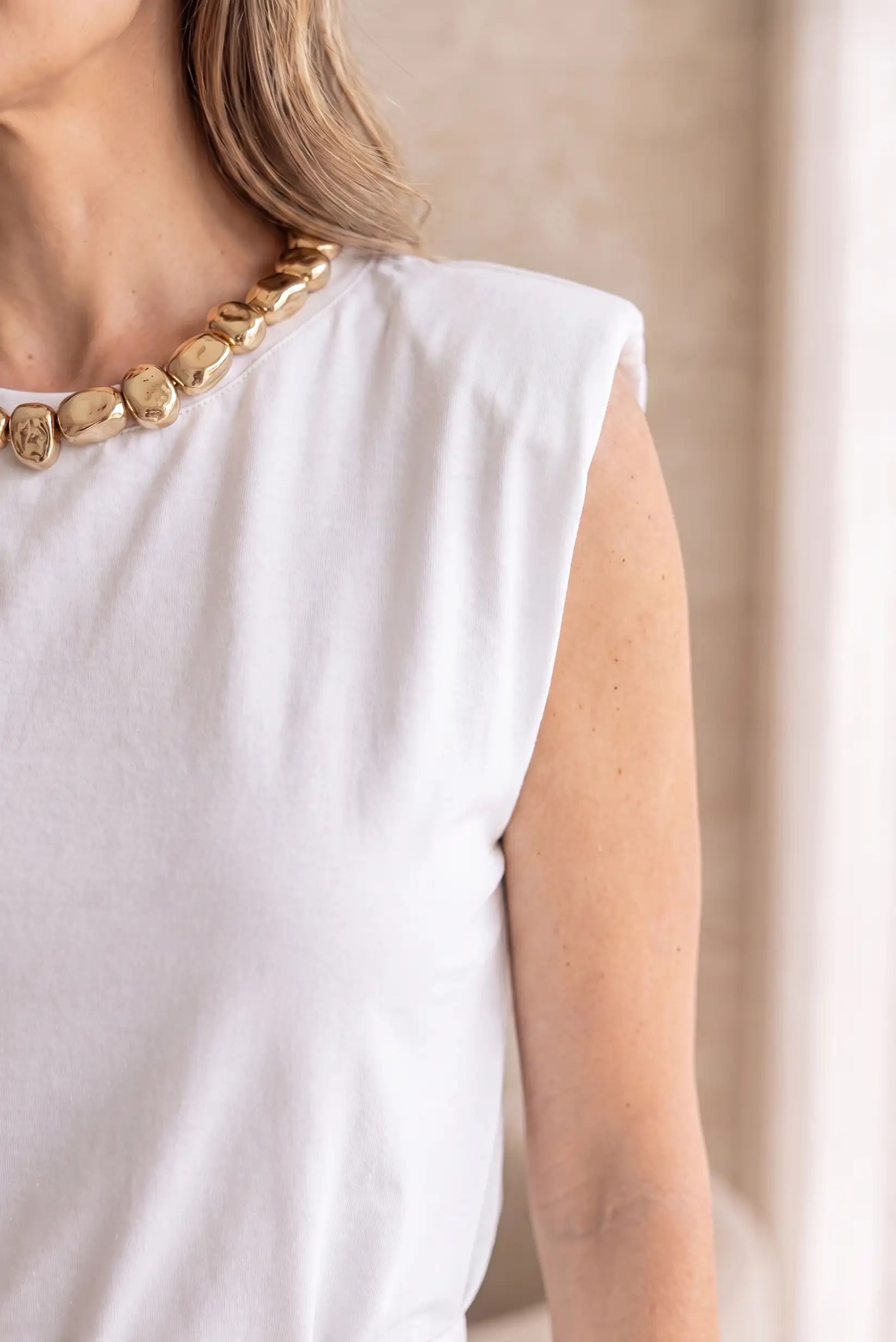Camiseta blanca sin mangas con collar dorado de perlas, moda femenina elegante y casual