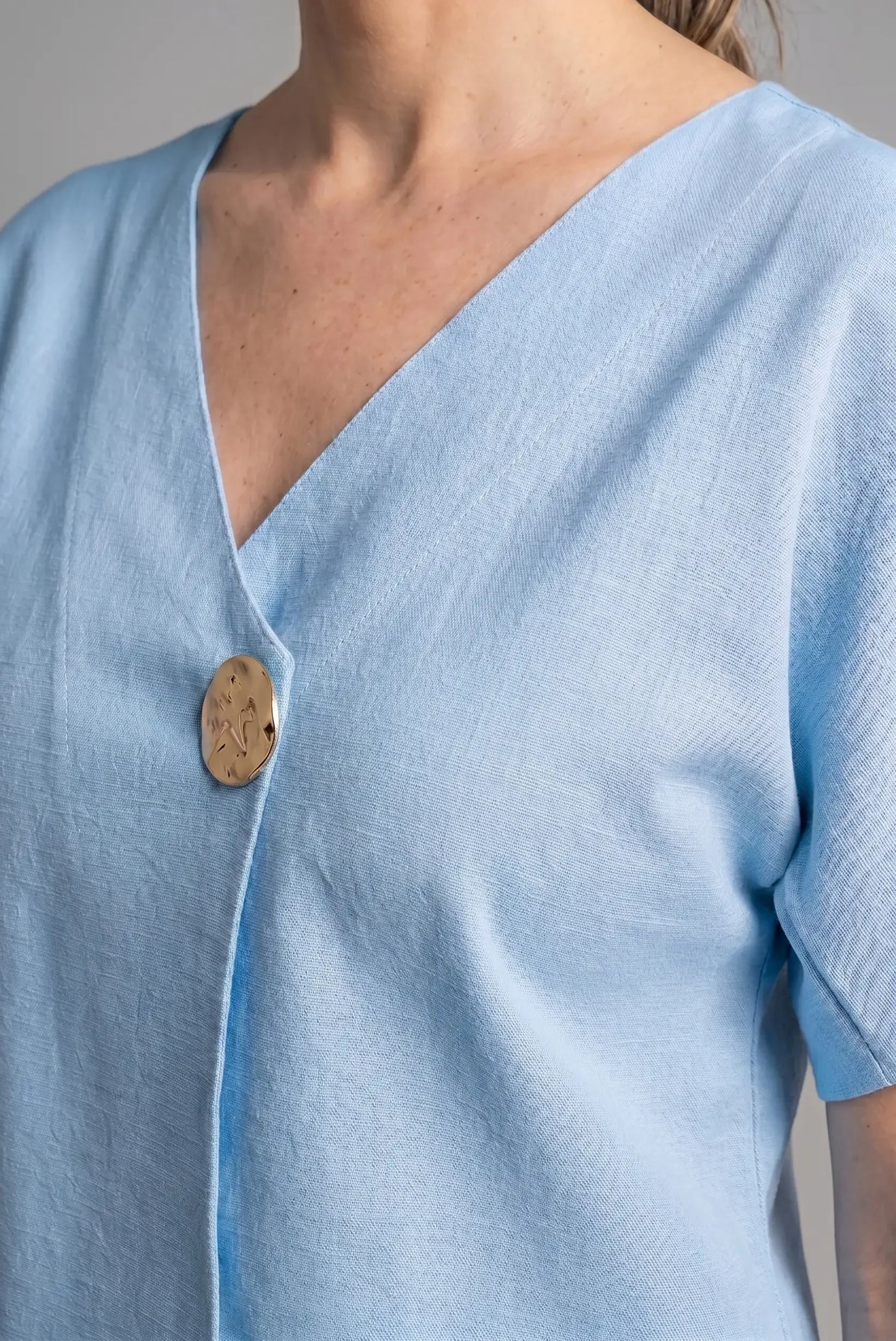 Camiseta azul cielo de manga corta con escote en pico y botón decorativo dorado.