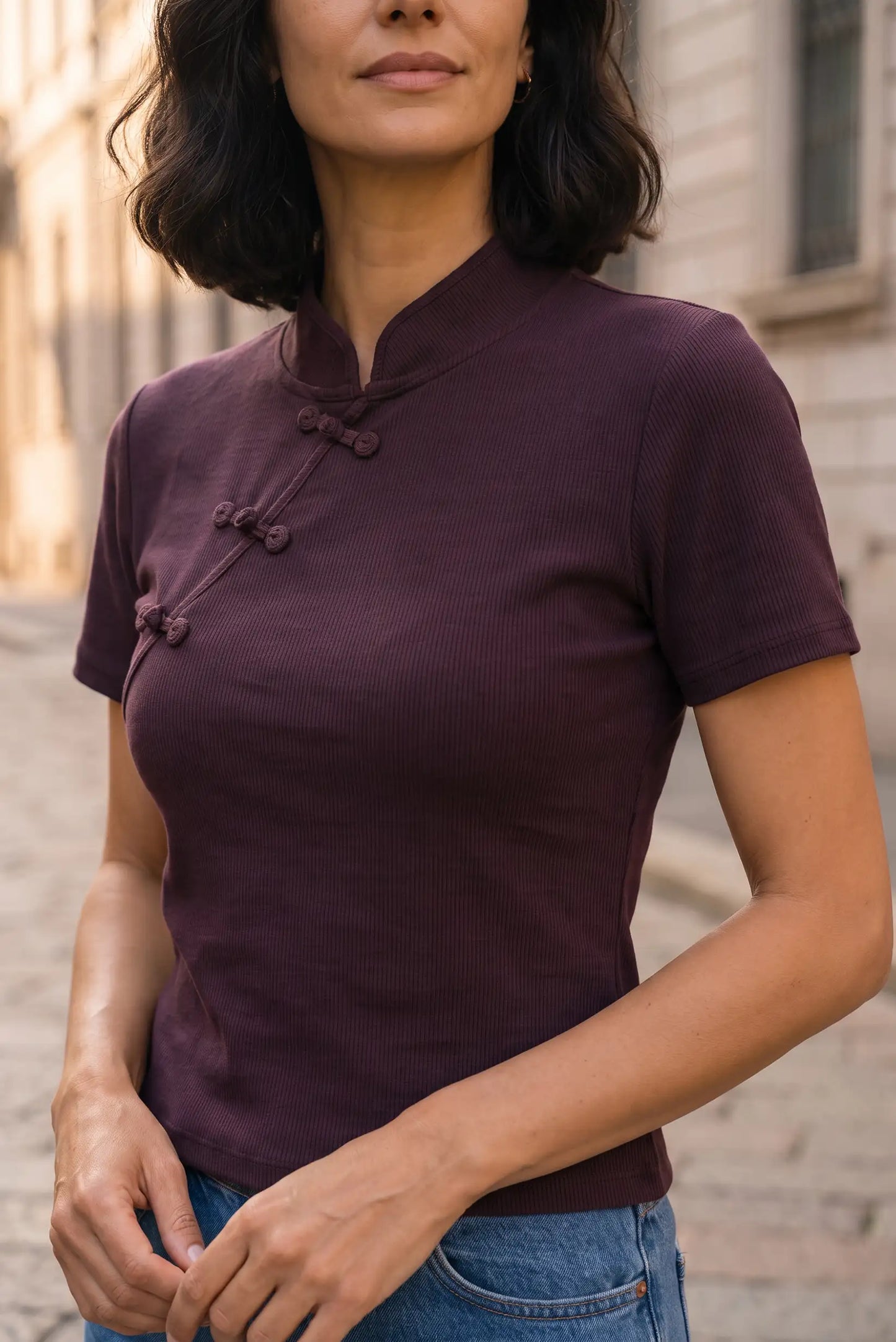 Mujer vistiendo camiseta ajustada color burdeos con cuello mandarín y botones chinos.