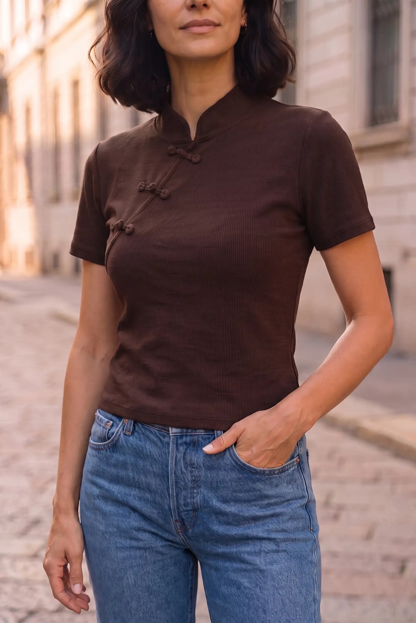 Mujer vistiendo camiseta marrón de manga corta con cierre de botones chinos y vaqueros azules.