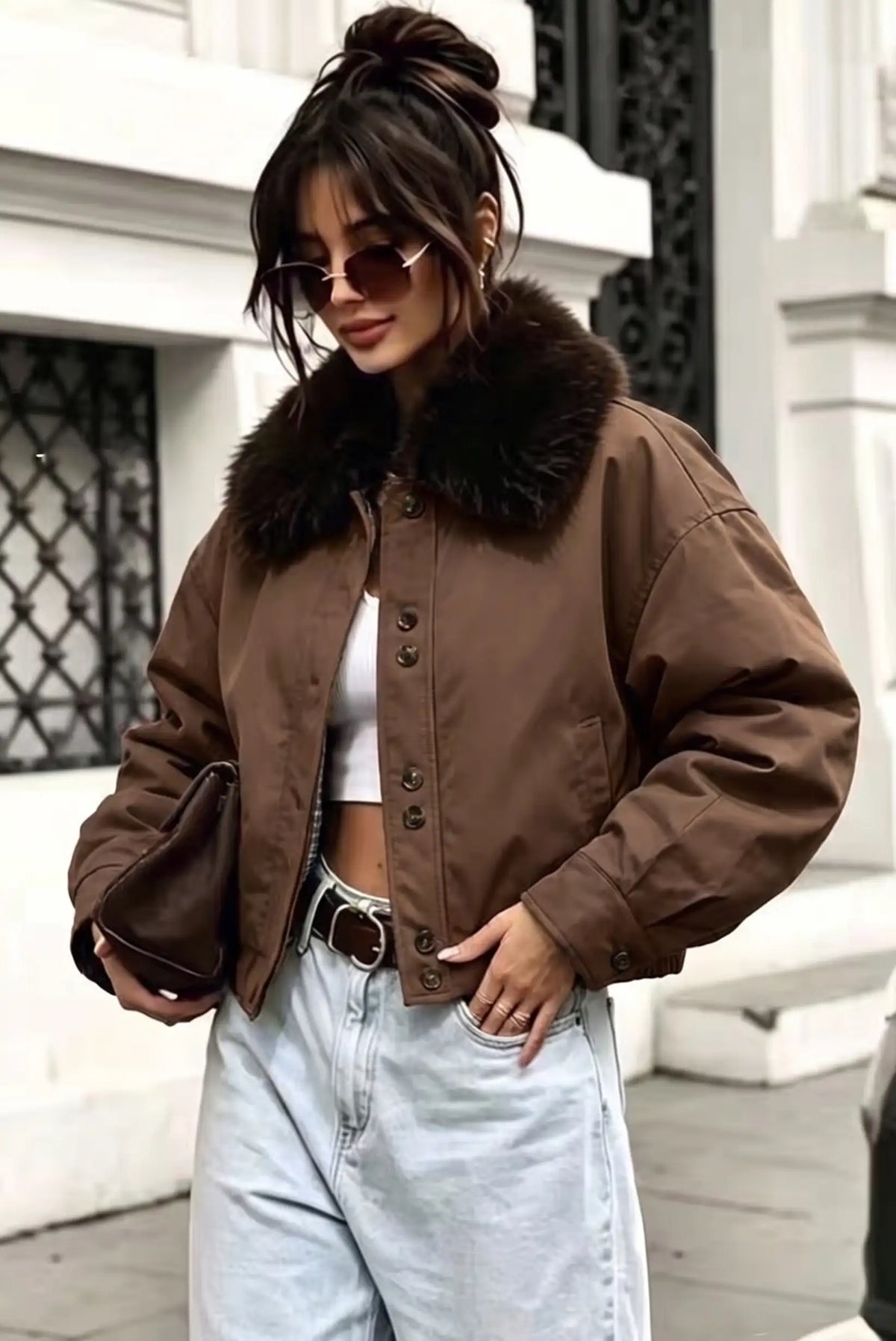 Mujer con chaqueta marrón corta con cuello de piel, top blanco y vaqueros claros.