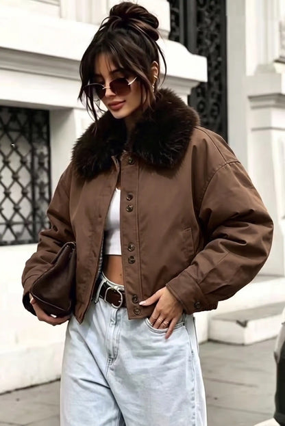 Mujer con chaqueta marrón corta con cuello de piel, top blanco y vaqueros claros.