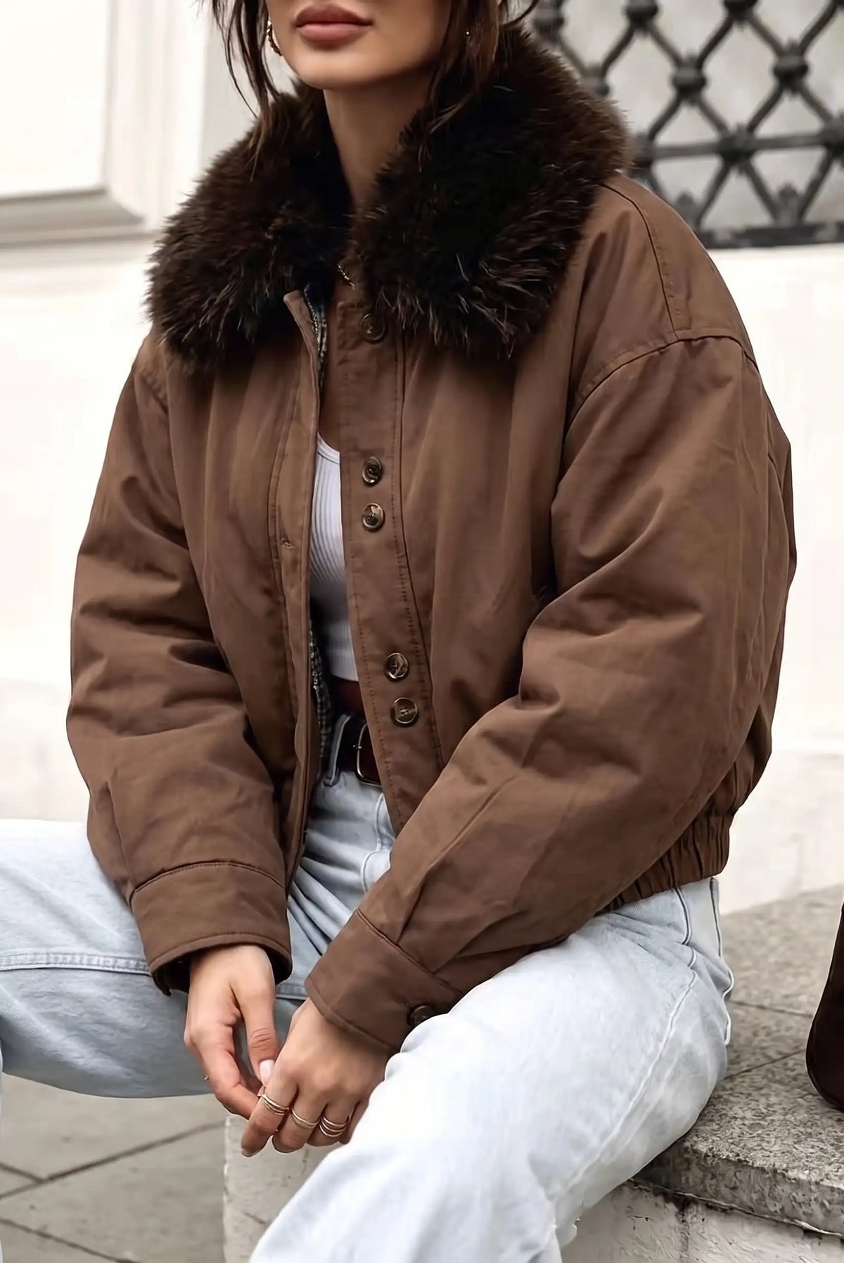 Mujer vistiendo chaqueta bomber marrón con cuello de pelo sintético y jeans claros.