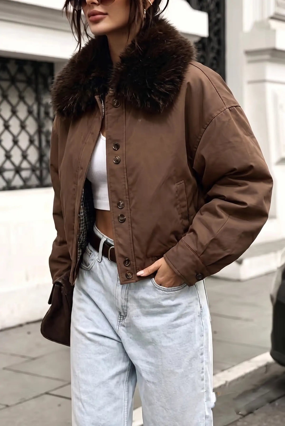 Mujer vistiendo chaqueta corta marrón con cuello de pelo sintético y jeans claros.