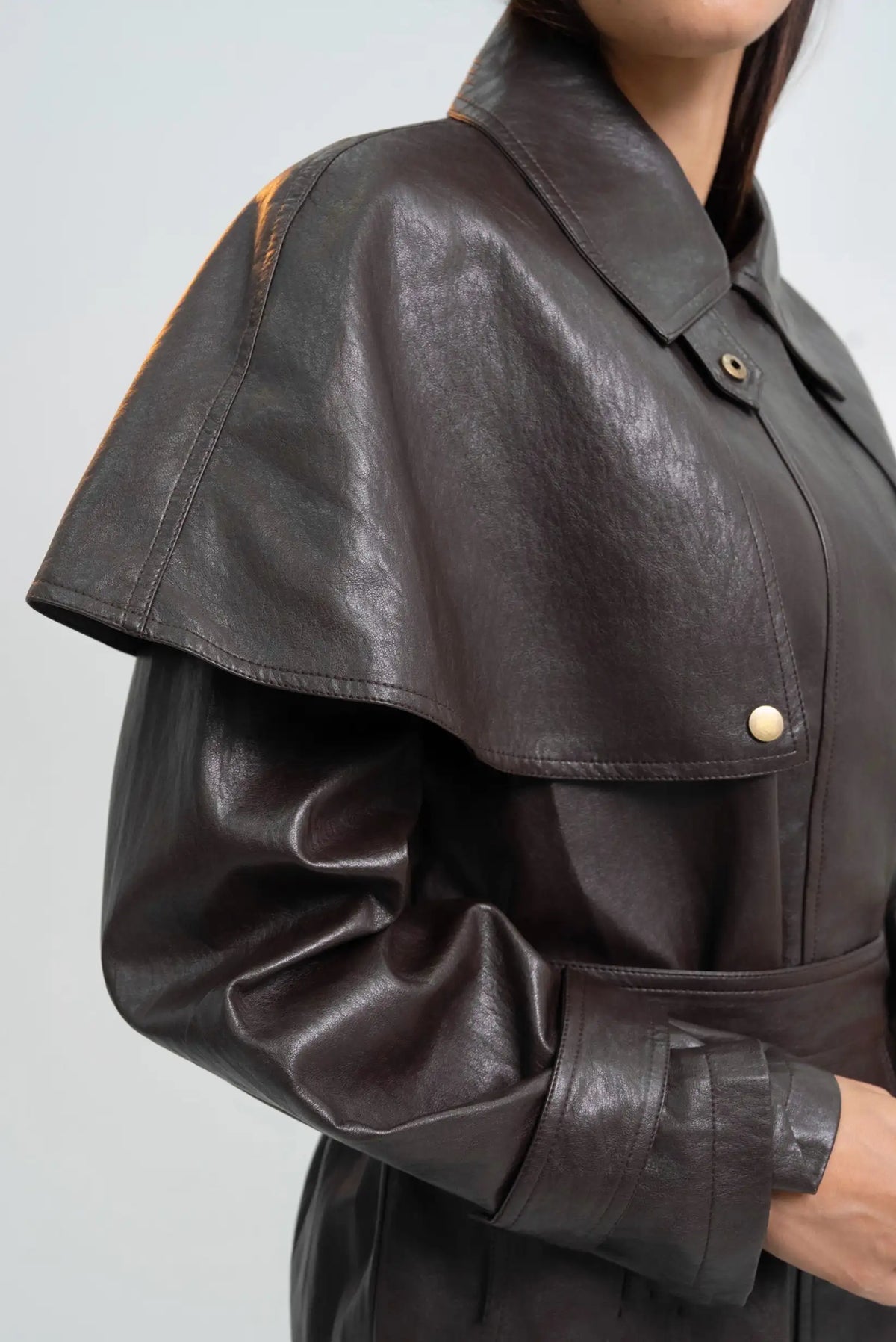 Detalle de gabardina de cuero sintético marrón oscuro para mujer