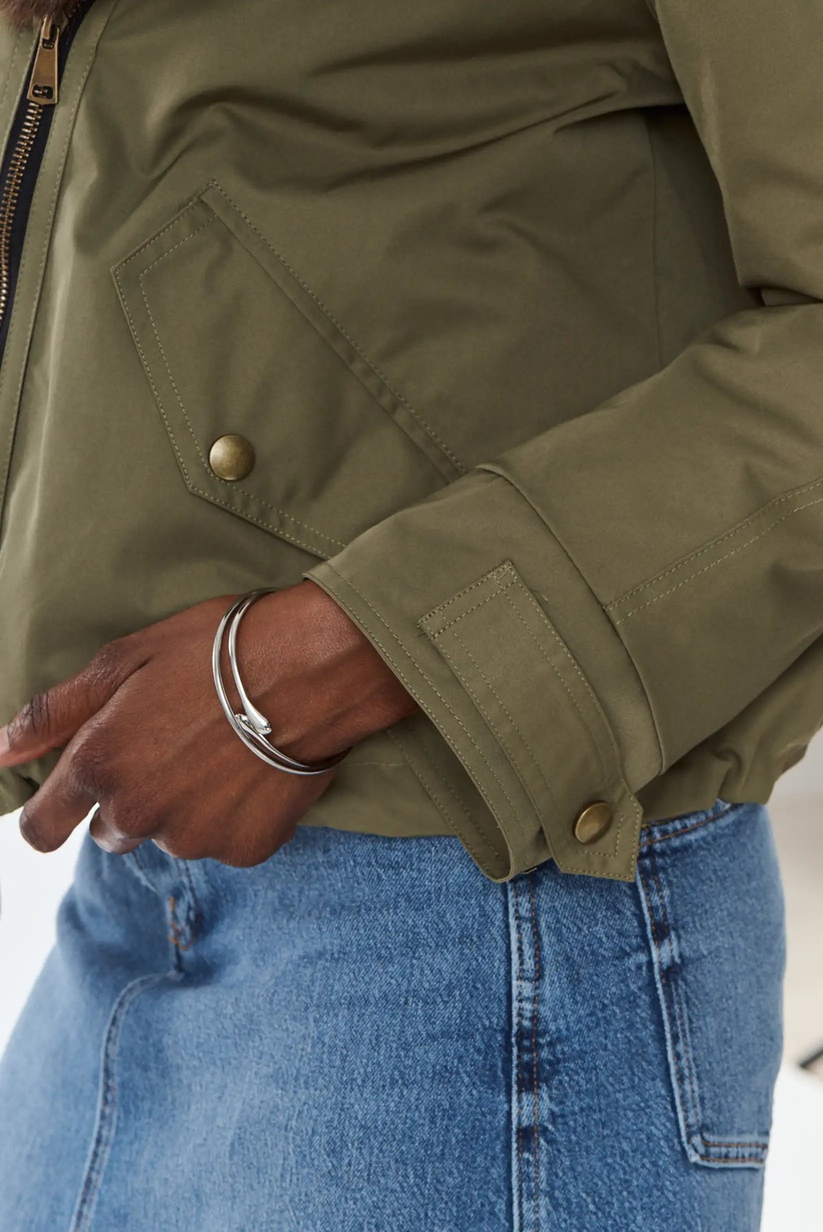 Detalle de pulsera rígida plateada con chaqueta verde oliva y falda vaquera.