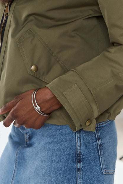 Detalle de pulsera rígida plateada con chaqueta verde oliva y falda vaquera.