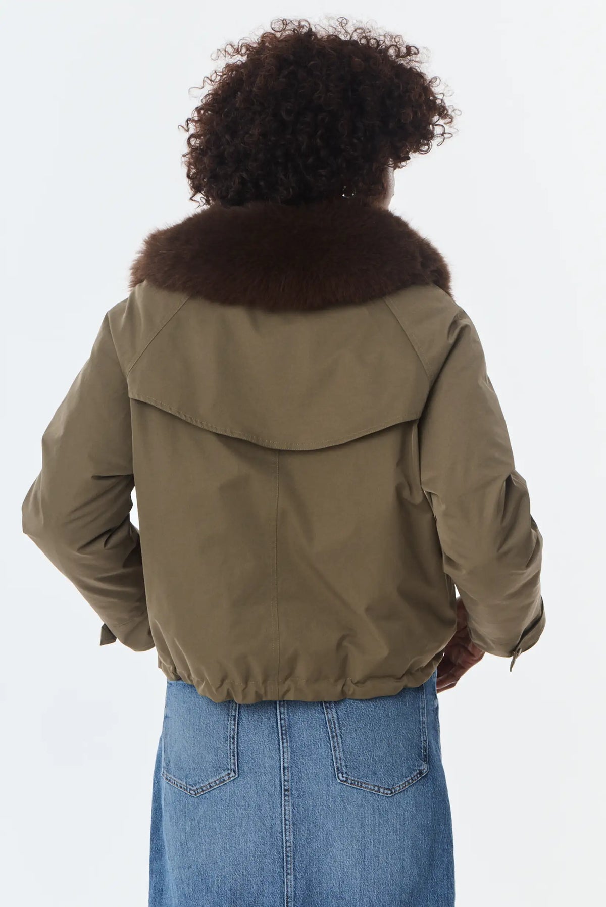 Vista trasera de mujer con chaqueta verde oliva con cuello de pelo marrón y falda vaquera