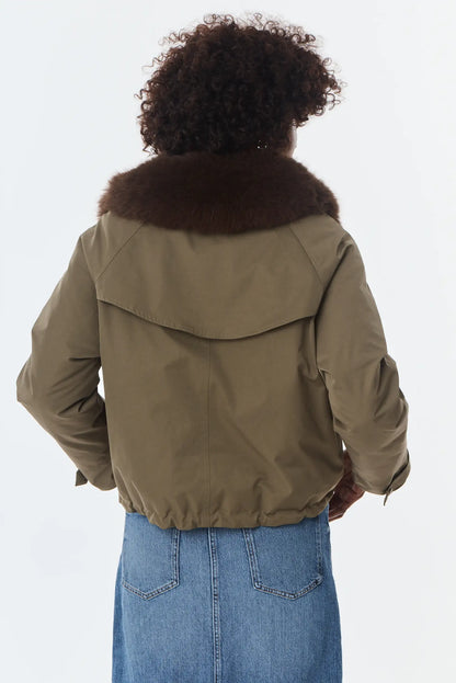 Vista trasera de mujer con chaqueta verde oliva con cuello de pelo marrón y falda vaquera