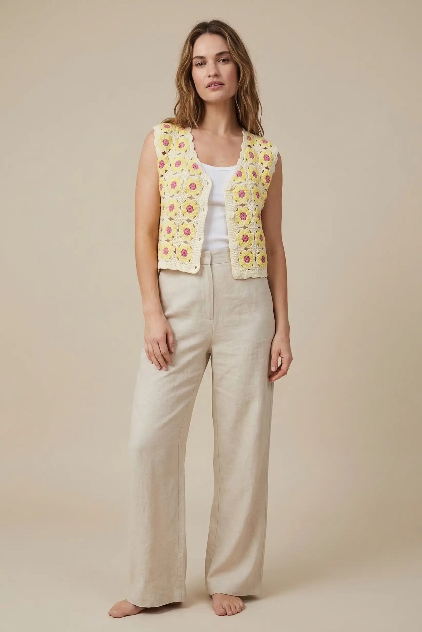 Mujer con chaleco de crochet amarillo con flores, pantalón beige y camiseta blanca, moda primavera.
