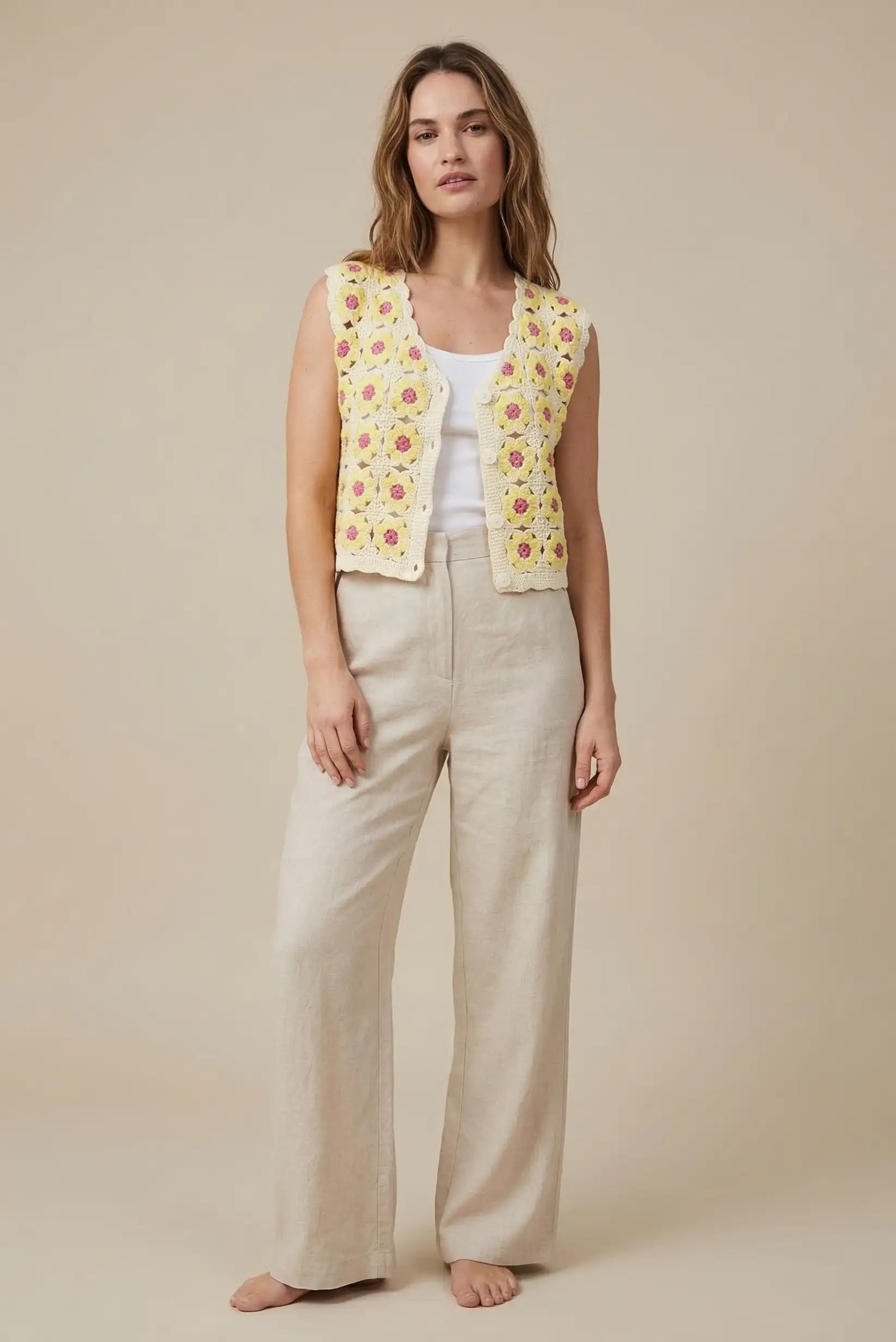 Mujer con chaleco de crochet amarillo con flores, pantalón beige y camiseta blanca, moda primavera.