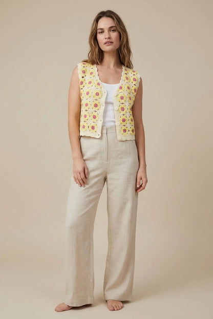 Mujer con chaleco de crochet amarillo con flores, pantalón beige y camiseta blanca, moda primavera.