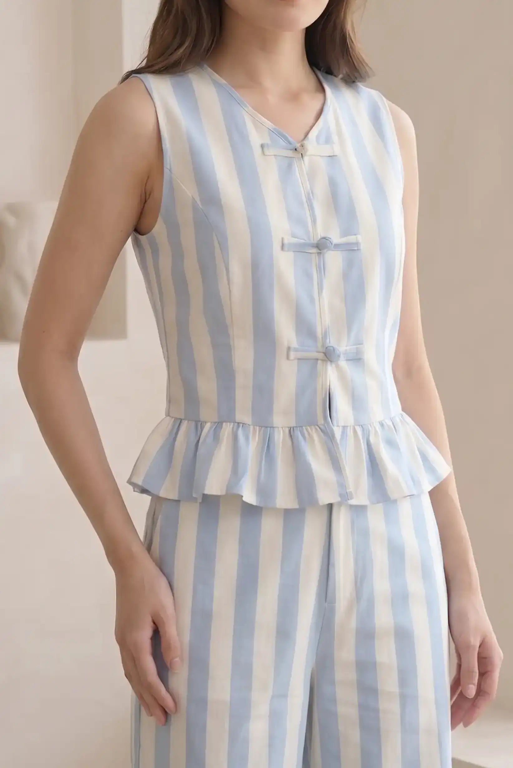 Chaleco de mujer sin mangas con rayas azul y blanco, detalle de volantes y botones decorativos.