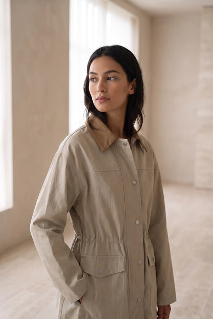 Mujer joven vistiendo una gabardina beige de corte moderno y minimalista.