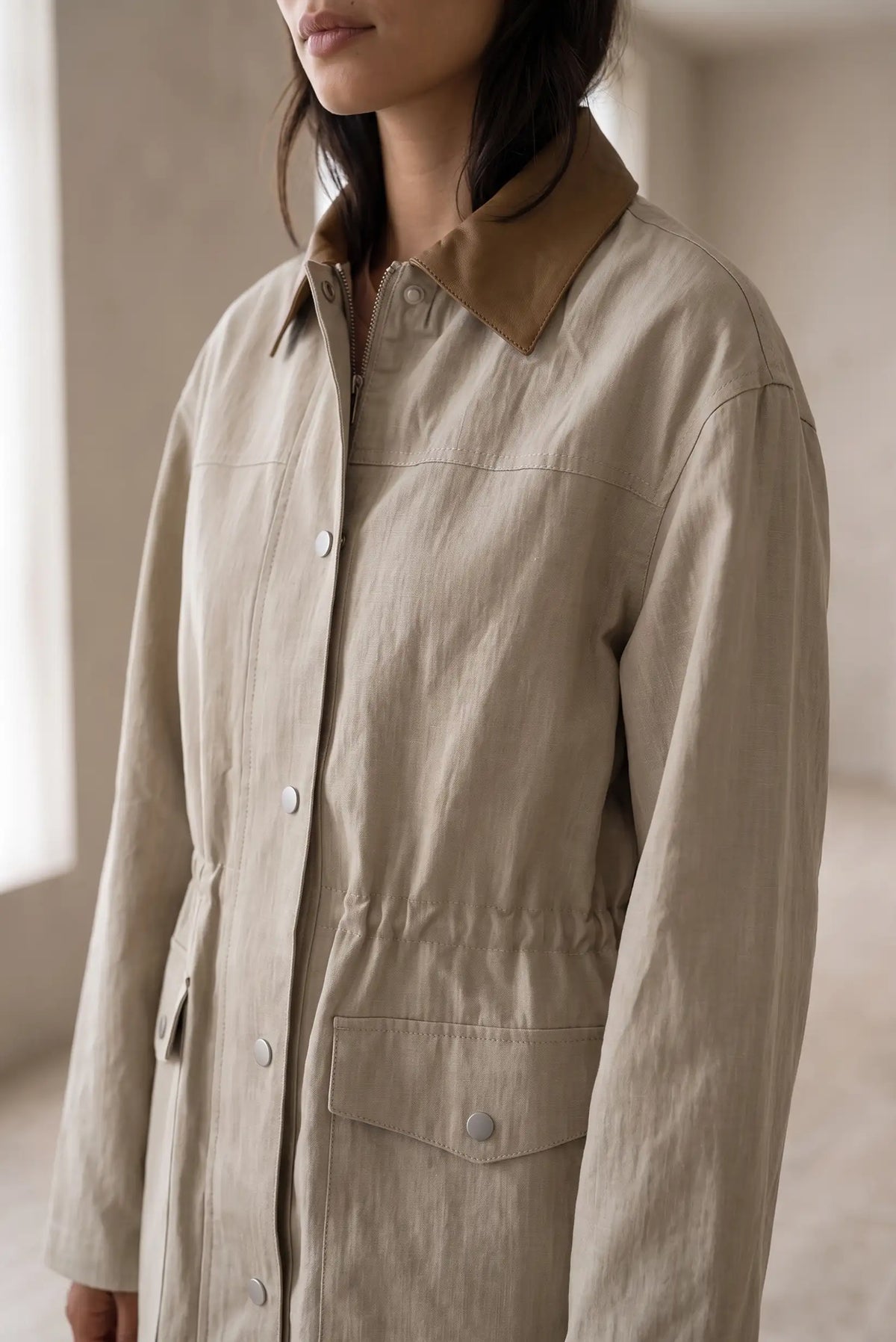 Mujer vistiendo una gabardina de lino beige con cuello marrón y cintura ajustable.