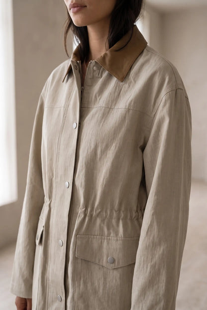 Mujer vistiendo una gabardina de lino beige con cuello marrón y cintura ajustable.