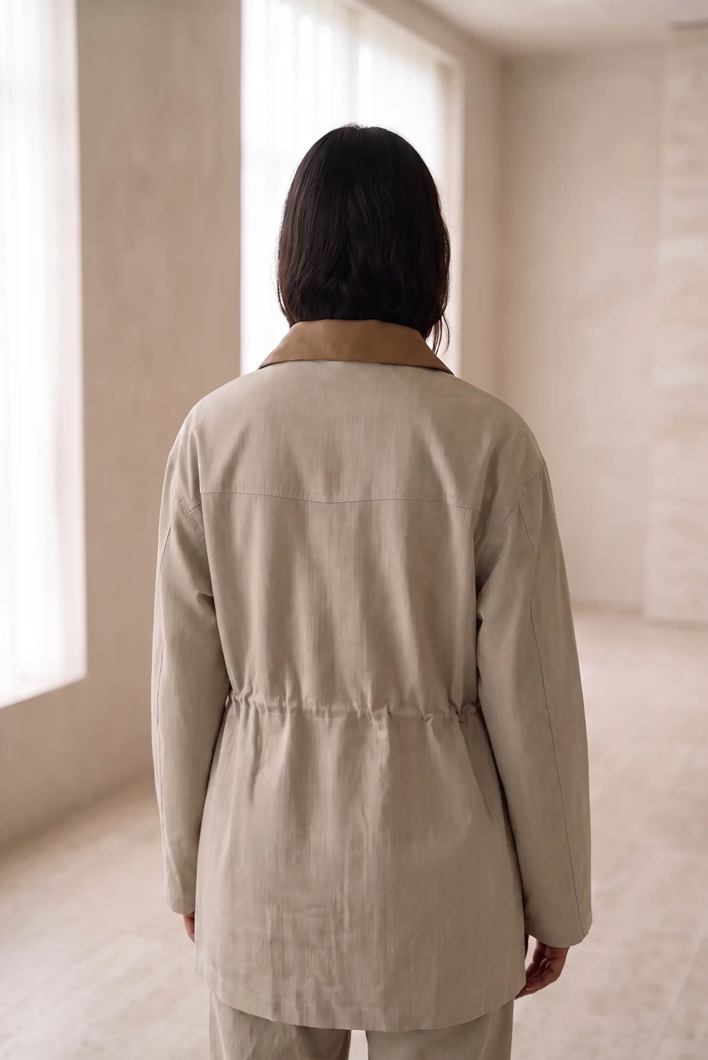 Mujer de espaldas vistiendo una chaqueta beige de corte relajado y cuello contrastado.
