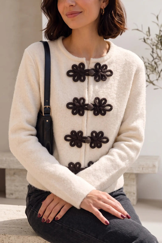 Mujer vistiendo chaqueta beige estilo Napoleón de CHICA del Sur con cierres decorativos negros.