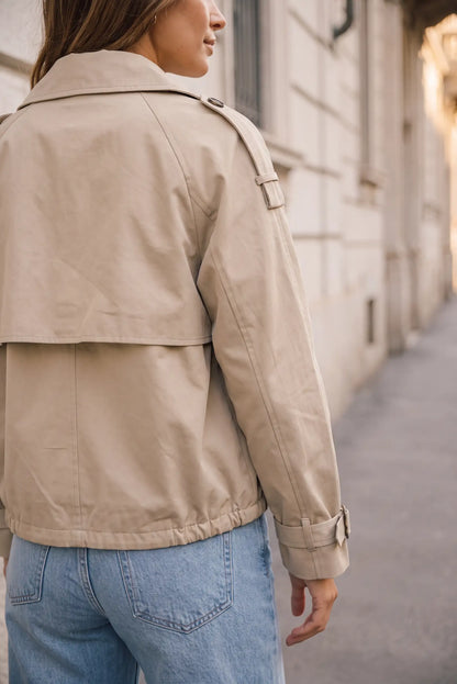 Mujer de espaldas vistiendo una chaqueta beige y vaqueros azules en una calle.
