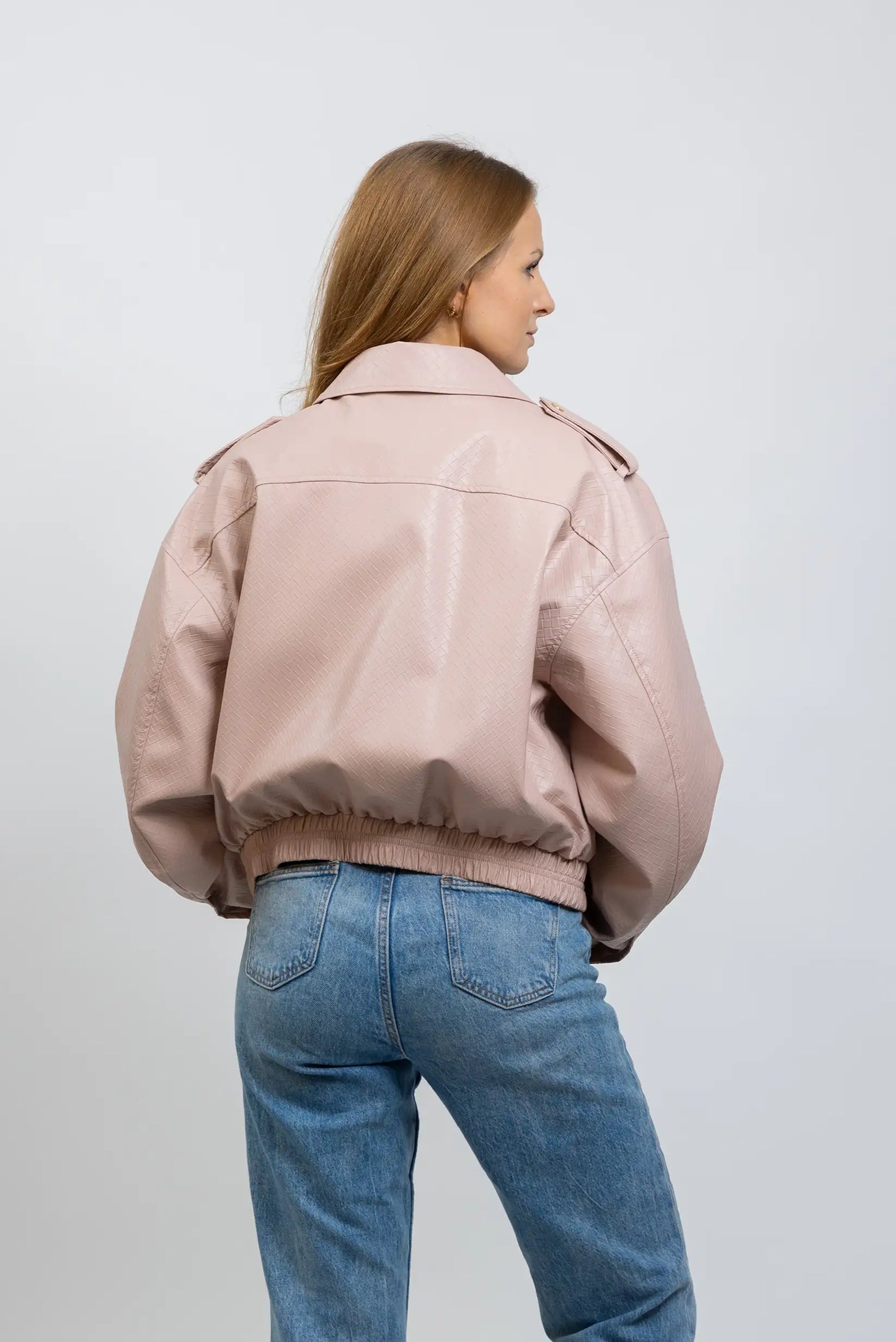 Mujer con chaqueta de polipiel rosa claro y jeans azules, vista trasera, moda casual