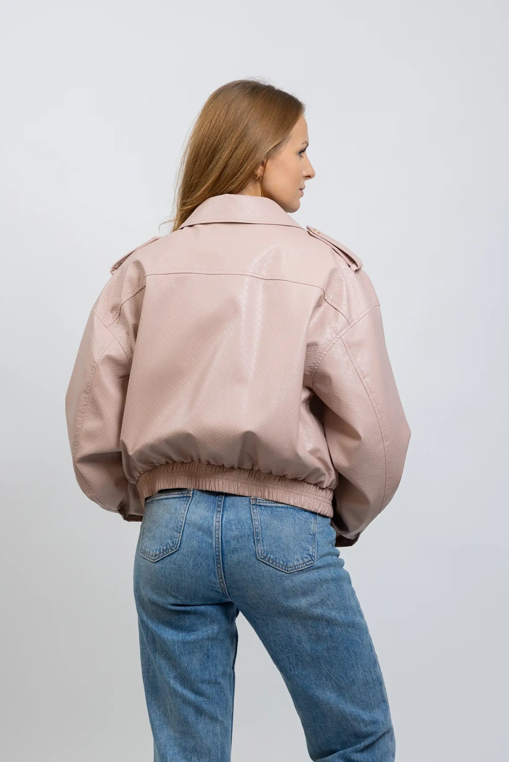 Mujer con chaqueta de polipiel rosa claro y jeans azules, vista trasera, moda casual