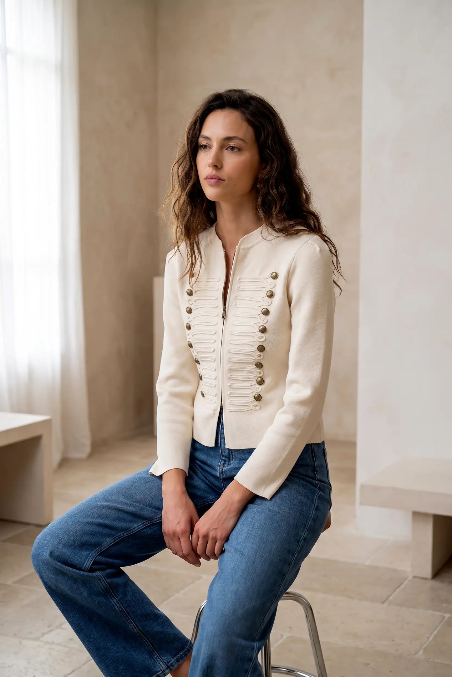 Mujer con chaqueta blanca estilo militar con botones dorados y vaqueros azules.