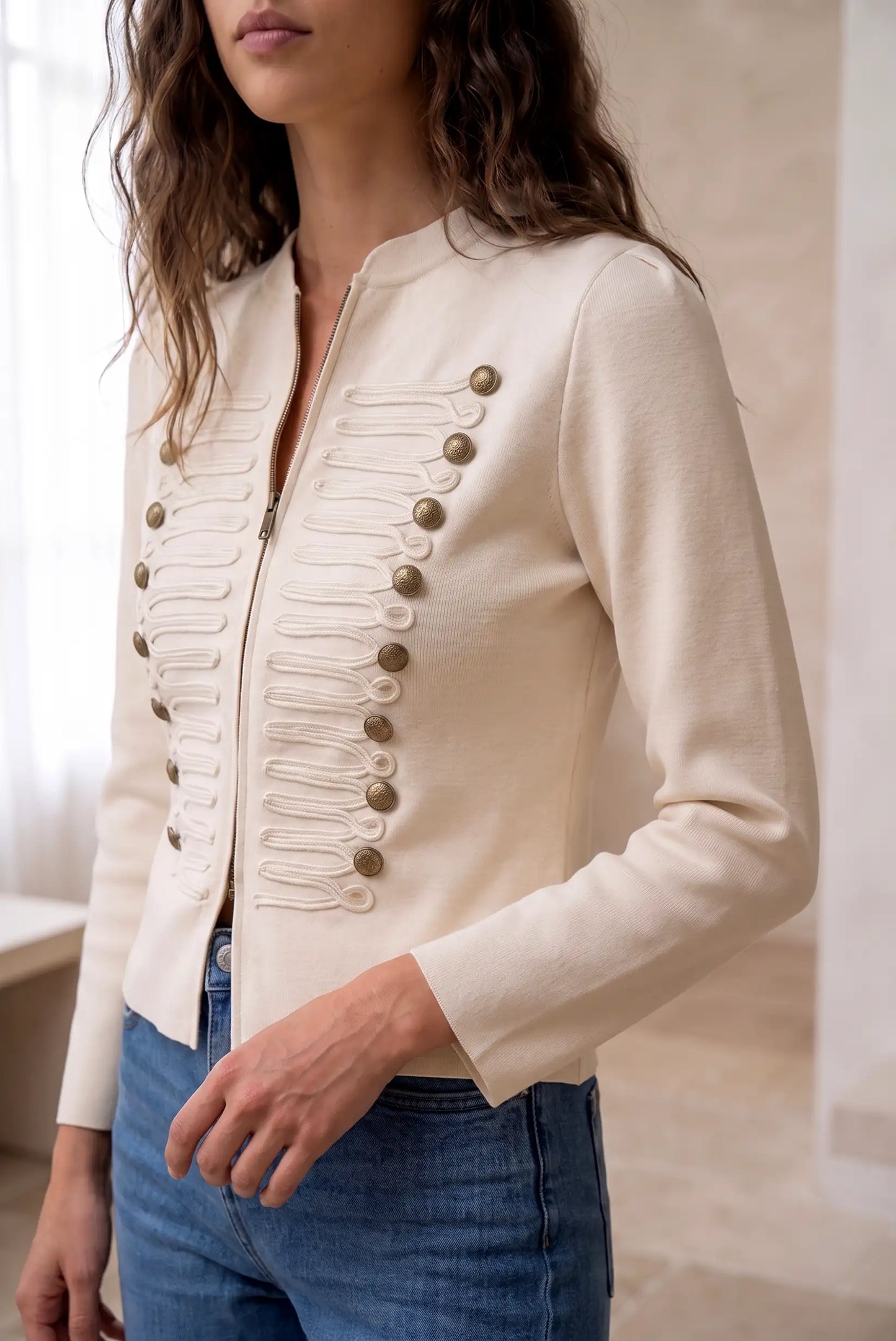 Mujer vistiendo chaqueta beige estilo militar con botones dorados y detalles bordados