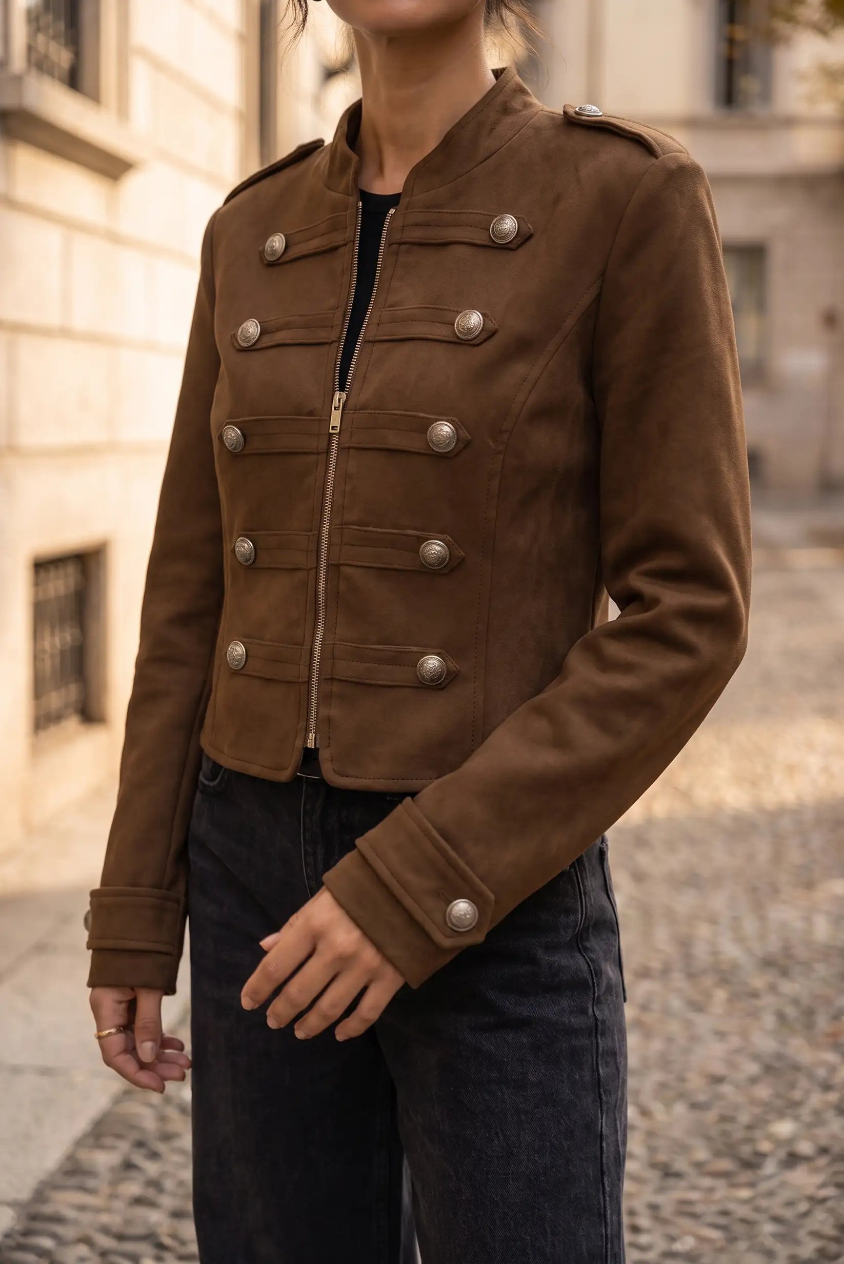 Chaqueta corta de ante marrón con botones metálicos decorativos y cierre de cremallera.
