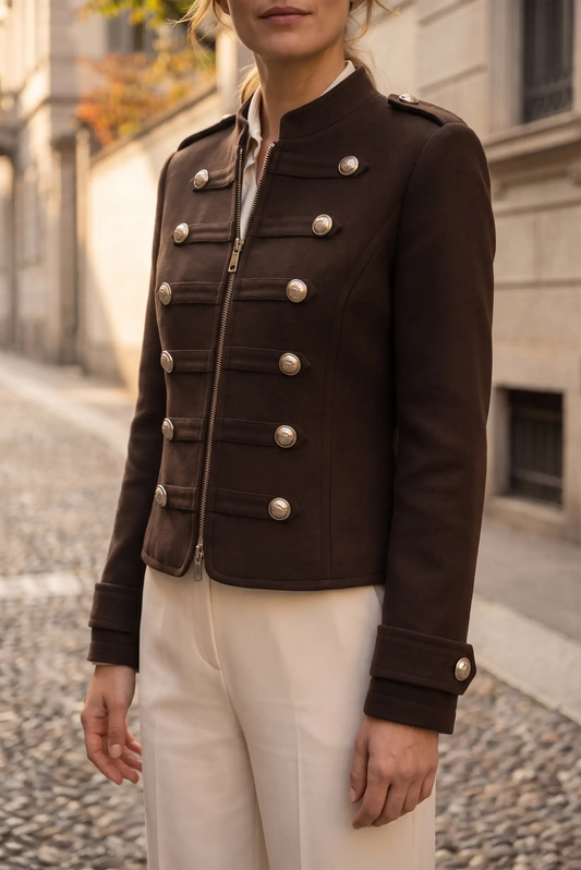 Mujer vistiendo chaqueta marrón estilo militar con botones plateados y pantalones blancos