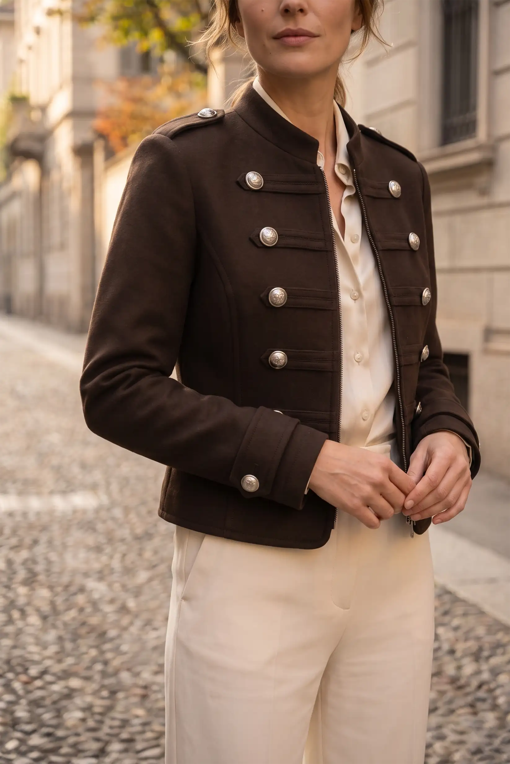 Mujer vistiendo chaqueta militar marrón con botones plateados y pantalón blanco