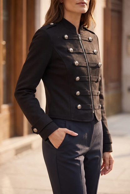 Mujer vistiendo chaqueta militar negra corta con botones plateados y pantalón oscuro.