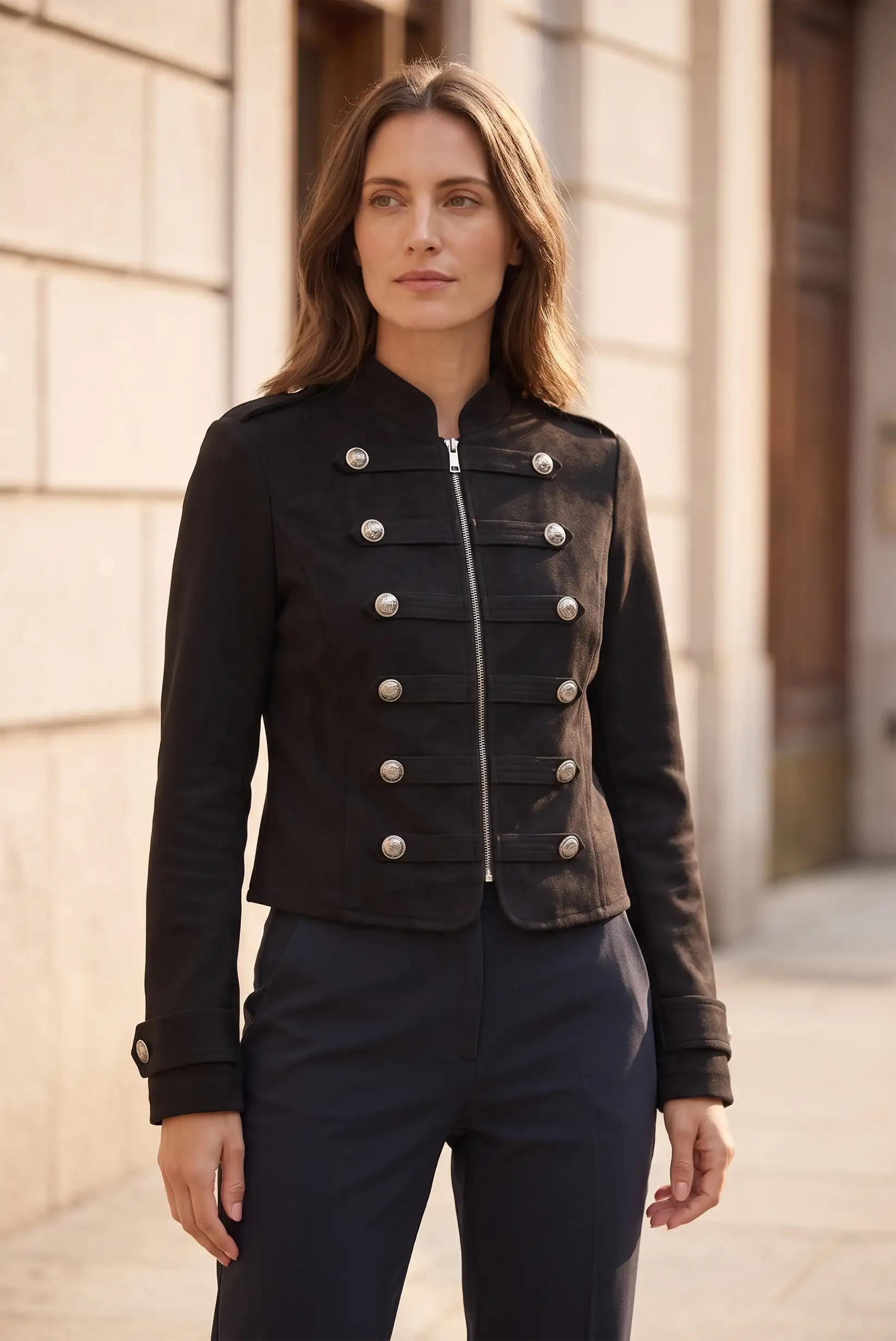 Mujer vistiendo chaqueta negra estilo militar con botones plateados y pantalones azul marino.