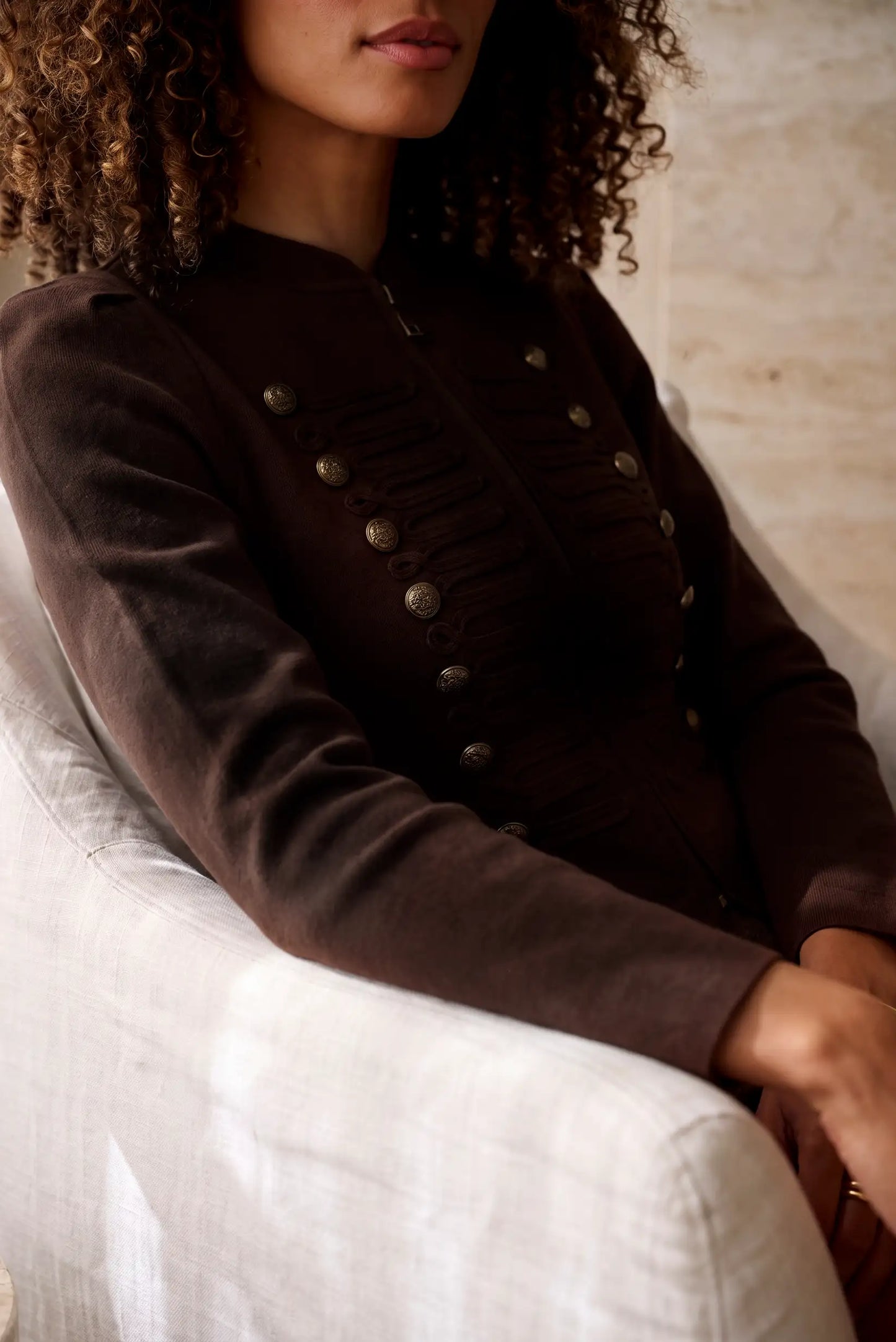 Mujer vistiendo una chaqueta marrón oscura con detalles de botones metálicos y pliegues.