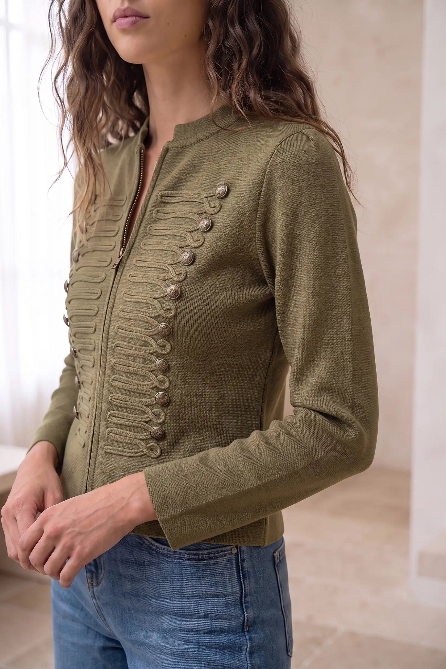 Chaqueta militar entallada color verde oliva con botones ornamentales y cierre frontal.