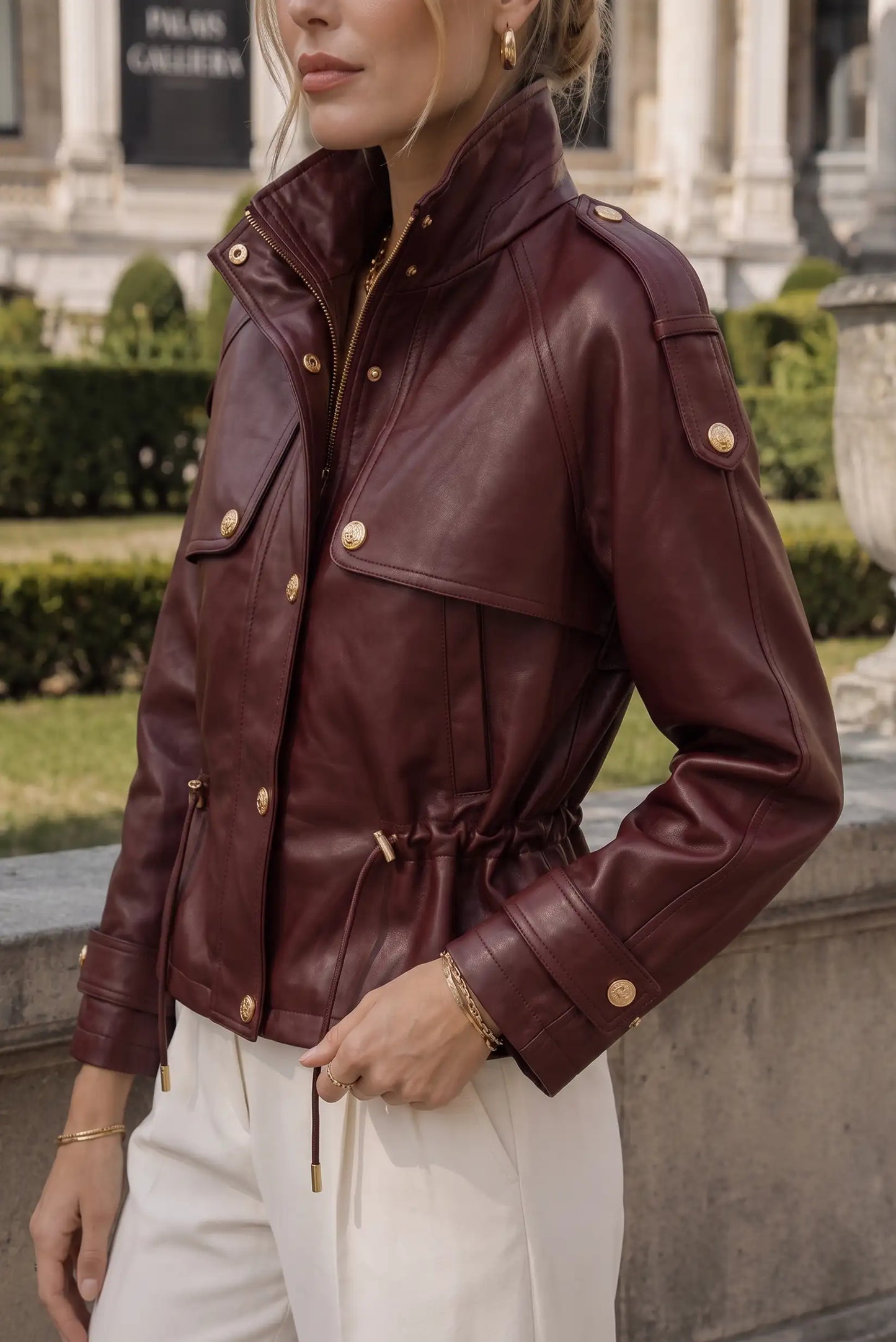 Chaqueta de cuero rojo vino con detalles dorados, cintura ajustable y bolsillos, ideal para moda femenina urbana.