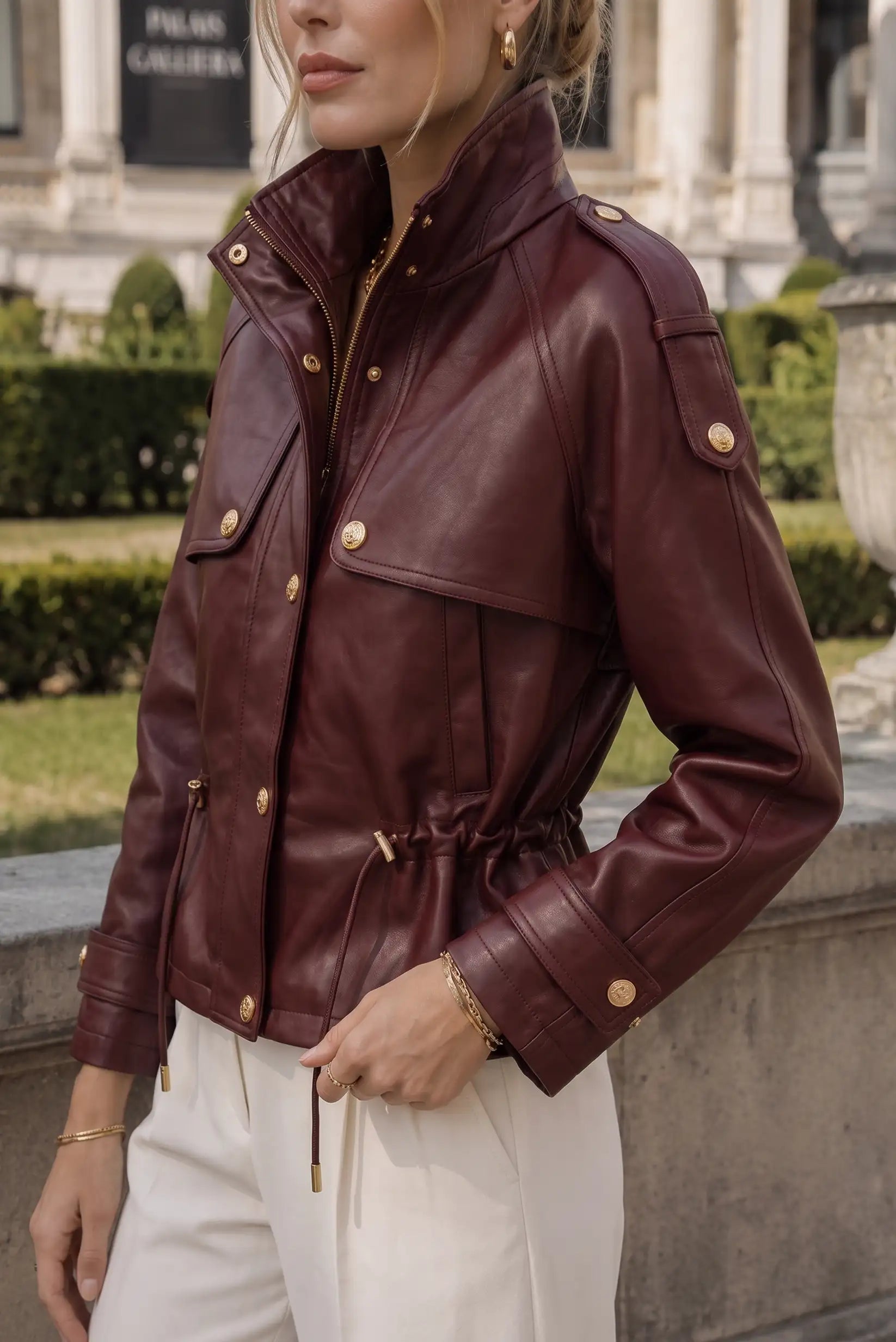 Chaqueta de cuero rojo vino con detalles dorados, cintura ajustable y bolsillos, ideal para moda femenina urbana.