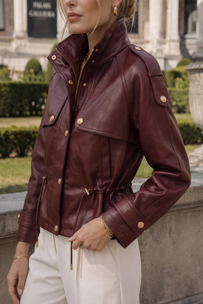 Chaqueta de cuero rojo vino con detalles dorados, cintura ajustable y bolsillos, ideal para moda femenina urbana.