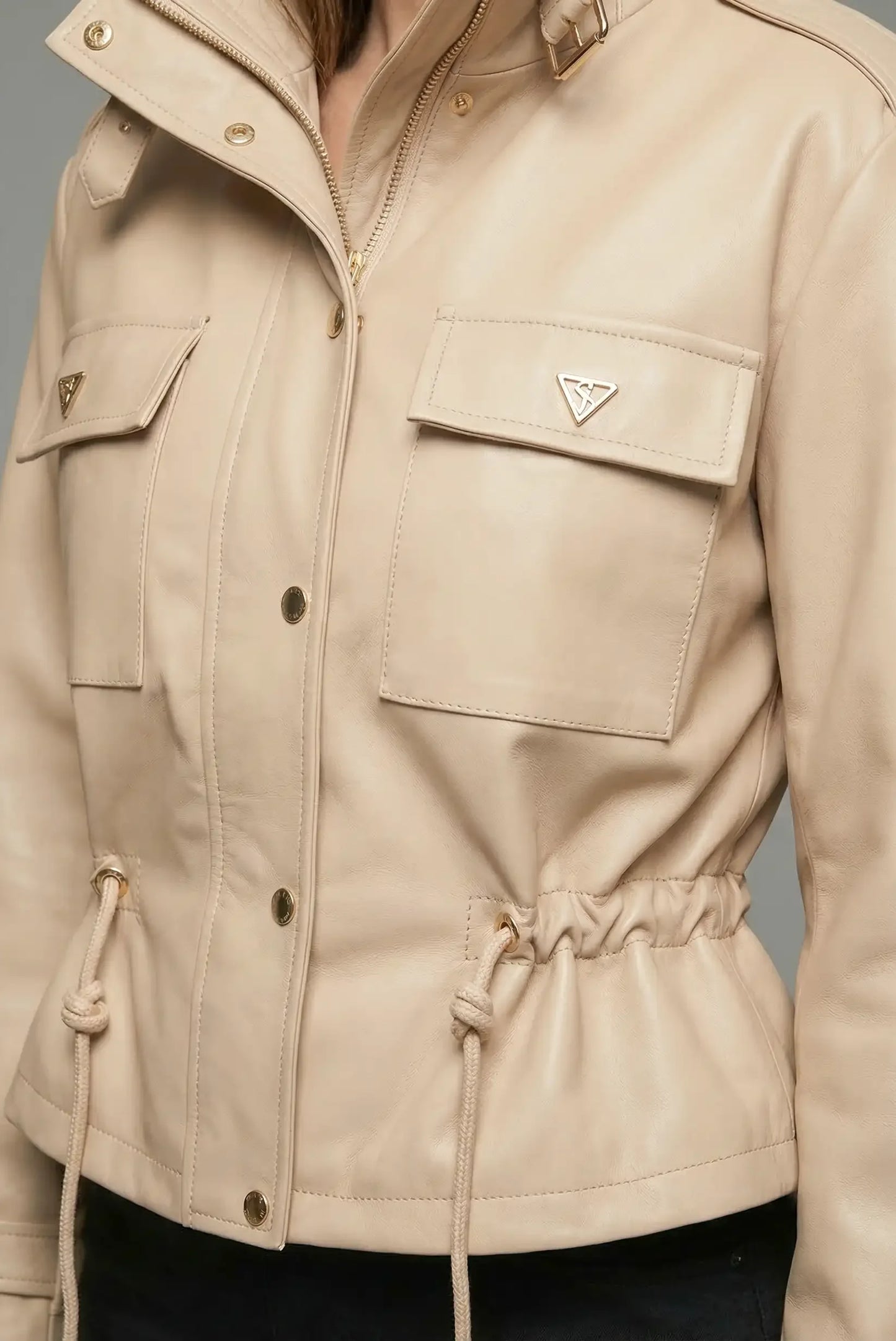 Chaqueta de mujer beige de polipiel, con bolsillos frontales y cierre de cremallera y botones.