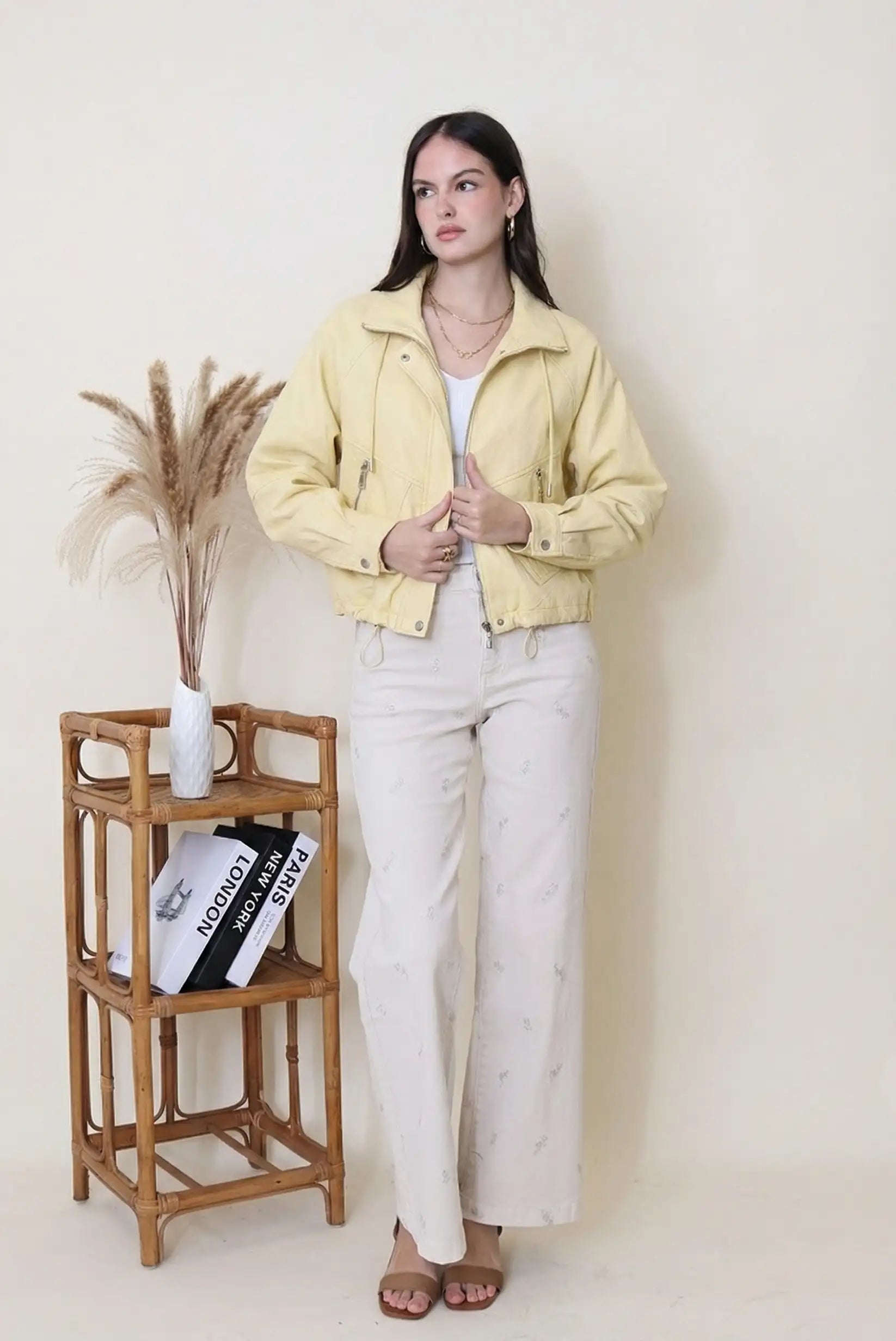Mujer con chaqueta amarilla de polipiel, pantalón claro y sandalias en ambiente minimalista