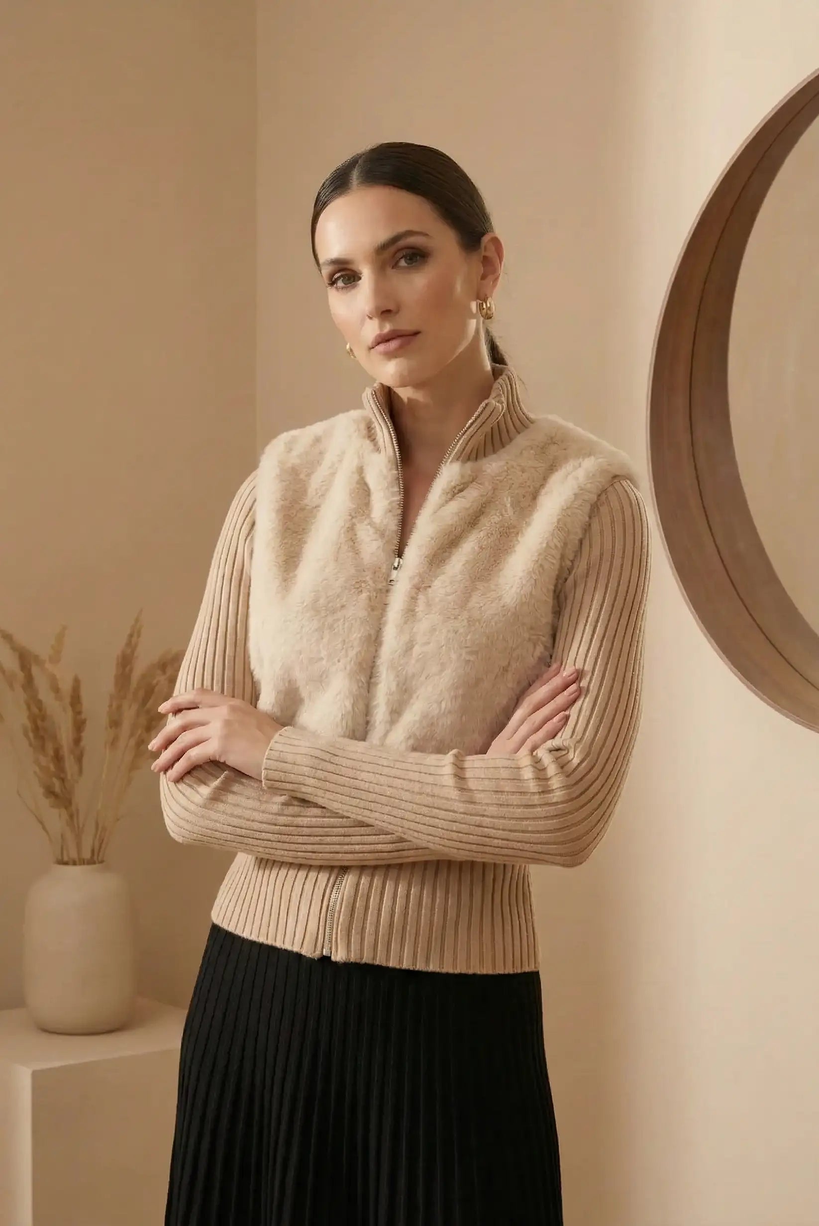 Mujer con chaqueta beige de pelo sintético y suéter de canalé en ambiente neutro con espejo redondo