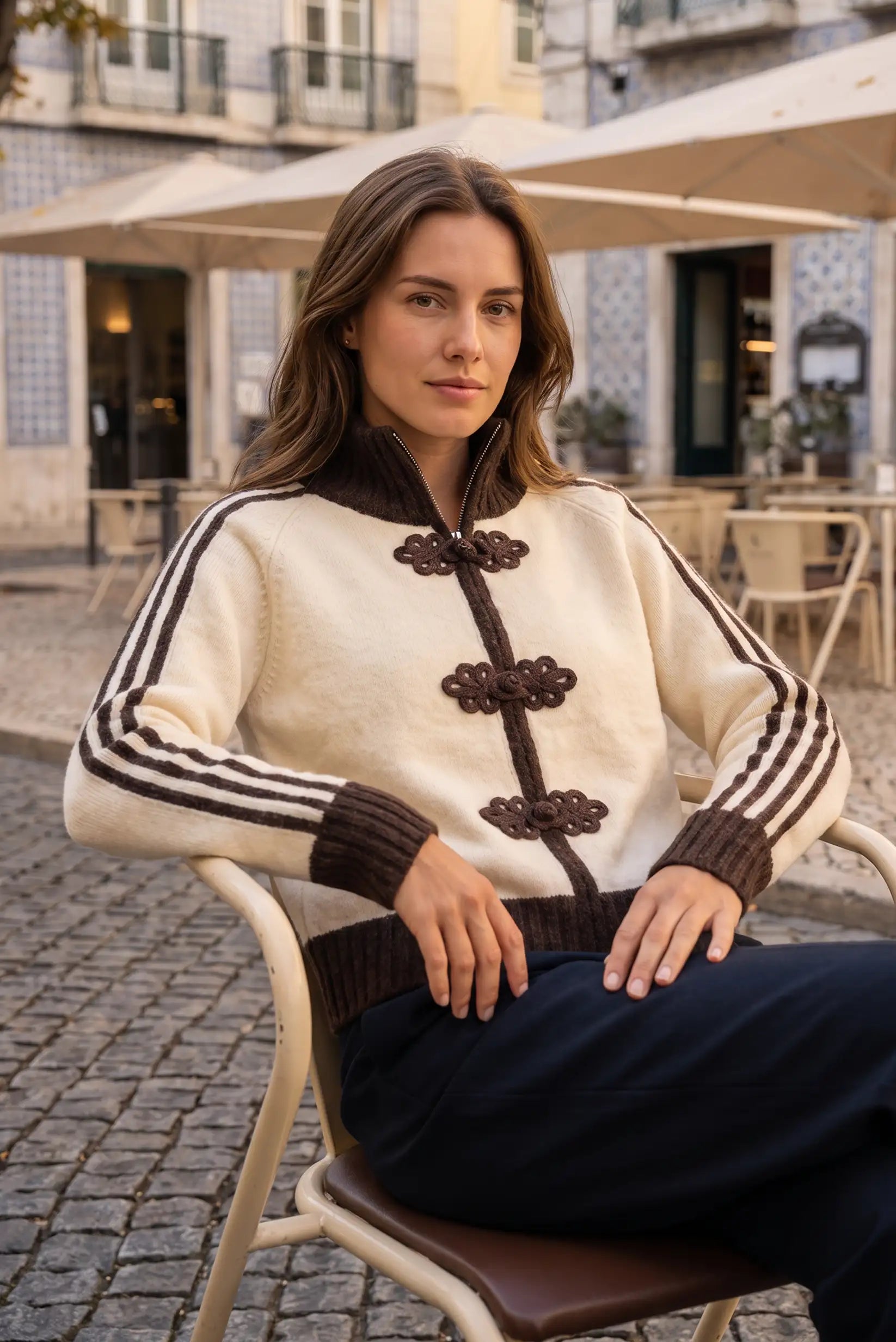 Mujer joven vistiendo un jersey beige con detalles marrones y botones ornamentales.