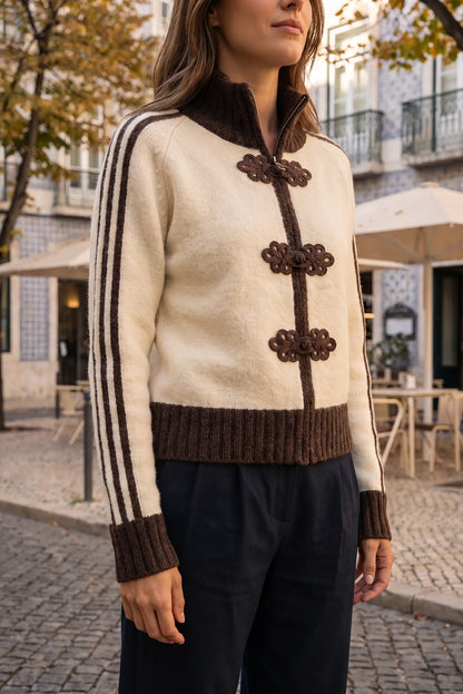 Mujer vistiendo jersey beige de punto con botones decorativos marrones y pantalones negros.
