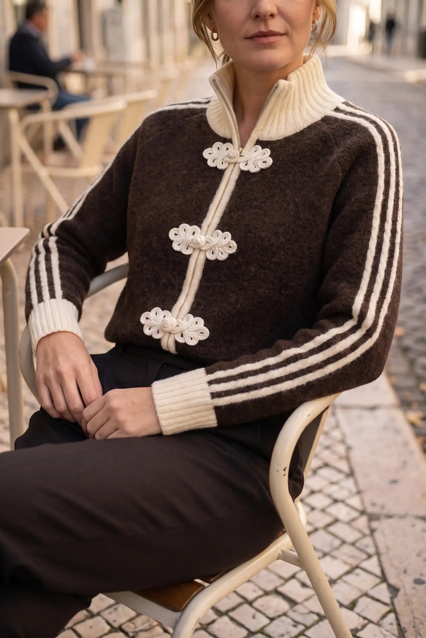 Mujer con jersey marrón de cuello alto, detalles florales blancos y rayas en las mangas.