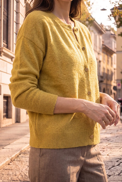Mujer vistiendo un cárdigan de punto amarillo mostaza con botones frontales.