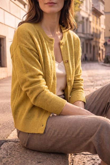 Mujer vistiendo rebeca de punto color mostaza y pantalones marrones en entorno urbano.