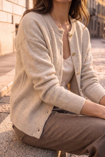 Mujer vistiendo una rebeca de punto color beige y pantalones marrones.